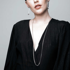 a woman wearing a long, minimal style,  sterling silver necklace with co-ordinating ball, drop earrings