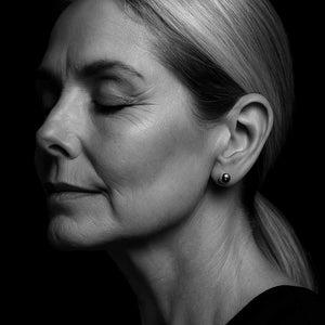 Elegant woman wearing minimalist silver ball stud earrings, captured in a close-up portrait against a black background, showcasing refined, timeless jewellery style.