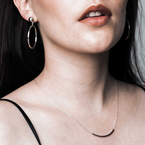 A timeless sterling silver jewelry set on a woman. Hoop earrings and a minimal style curved bar necklace.