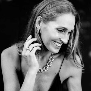 Woman smiling and wearing a handcrafted recycled sterling silver chain link statement necklace, along with matching earrings and rings. The necklace features bold custom links and a rolo chain for added texture.