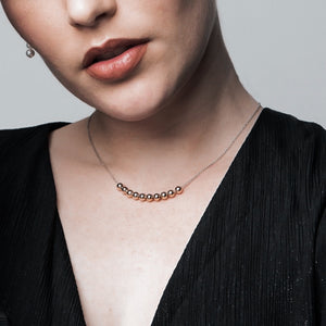 A woman wearing a delicate gold necklace that features 10 small, 9k gold balls on a short, delicate chain.