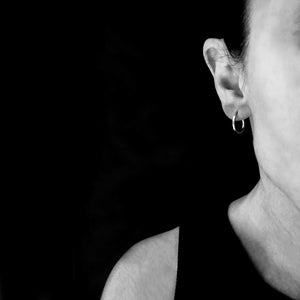 Close-up black and white image of a woman wearing minimalist small hoop earring, styled against a dark background.

