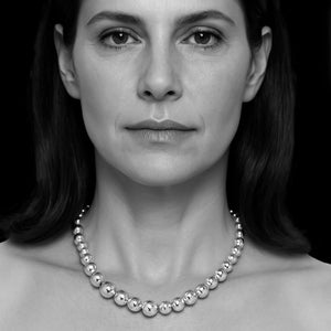 Black and white portrait of a woman wearing a multi ball necklace against a dark background