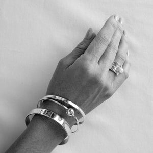 Hand wearing silver bracelets  and pearl ring stack on a plain background