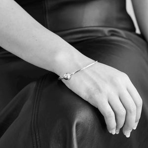 Woman gracefully showcasing the Single Ball Bangle crafted from recycled sterling silver, featuring a sliding ball on a flat-edged band for lightweight, elegant everyday wear.