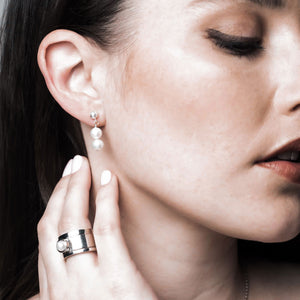 a woman wearing contemporary pearl drop earrings with a co-ordinating pearl ring stack.