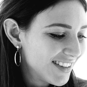 A woman smiling whilst wearing sterling silver hoop earrings that feature a  ball stud.