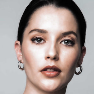 Stylish woman wearing SOPHIE ANNA gold tube hoop earrings, looking confidently to the camera.
