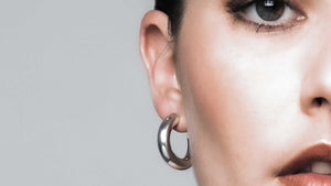 Close-up of a woman wearing Sophie Anna's sterling silver tube hoop earrings, showcasing their elegant design and shine against her skin.