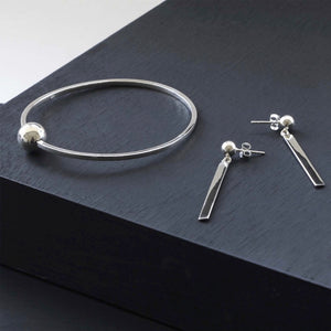 A timeless jewelry set with a silver bangle with a ball feature and drop bar earrings.
