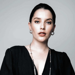 Woman exuding elegance while wearing SOPHIE ANNA tube hoop earrings and a ball and bar necklace, smiling at the camera.